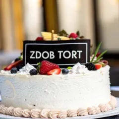 Biały tort udekorowany świeżymi owocami: truskawkami, borówkami i jeżynami.