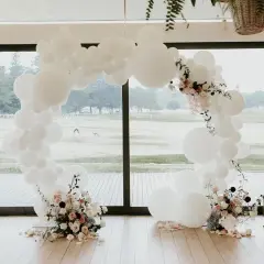 Okrągła girlanda z białych balonów ozdobiona kwiatami, obok beczki z tortem.