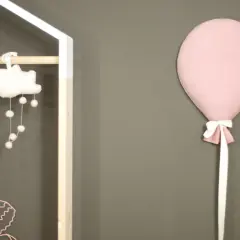 Różowy balon z kokardką przyczepiony do szarej ściany obok dziecięcej dekoracji.