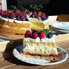 Tort biszkoptowy z kremem, malinami i borówkami, udekorowany miętą.