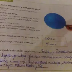Niebieski balon i fragment ręki trzymającej taśmę mierniczą na tle tekstu o doświadczeniu.