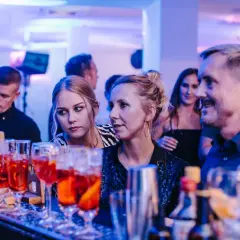 Ludzie przy barze, na pierwszym planie drinki, w tle niebieskie światła.
