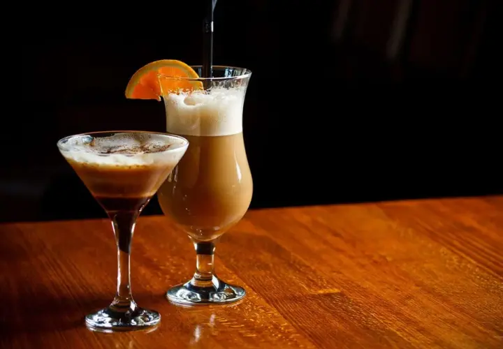 Dwa drinki kawowe: jeden w kieliszku martini, drugi w wysokiej szklance z pomarańczą.