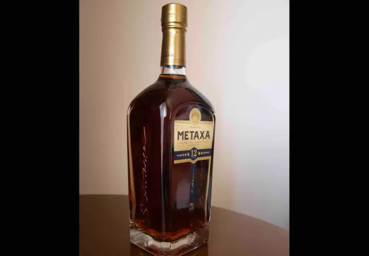 Butelka greckiego brandy Metaxa 12 gwiazdek na stole.