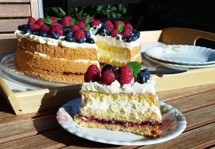 Tort biszkoptowy z kremem, malinami i borówkami, udekorowany miętą.