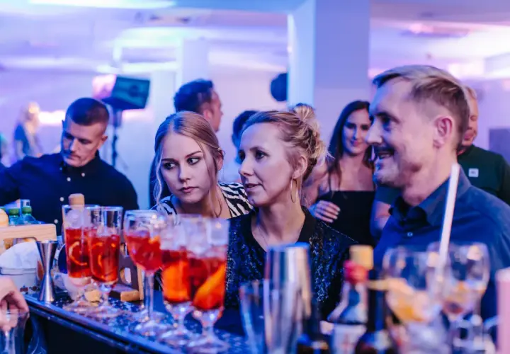 Ludzie przy barze, na pierwszym planie drinki, w tle niebieskie światła.