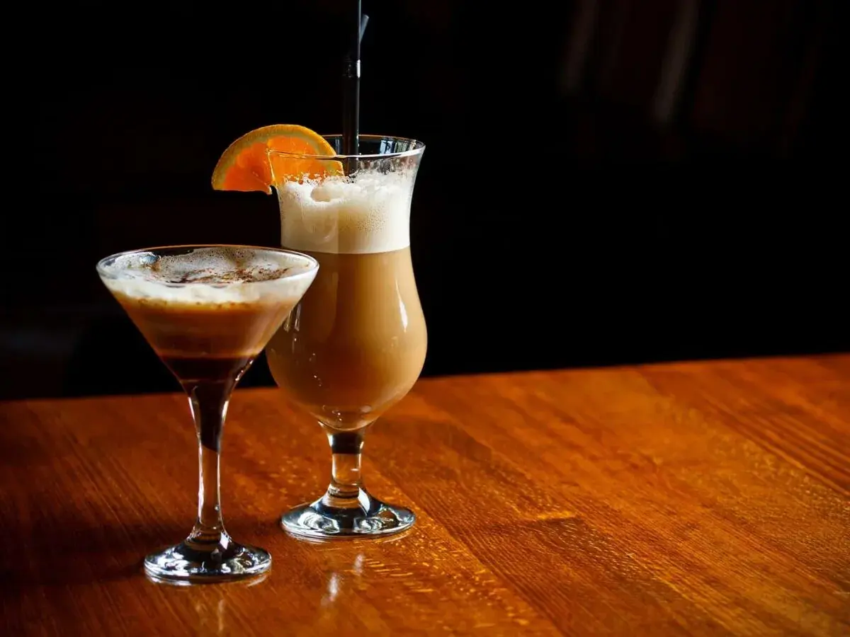 Dwa drinki kawowe: jeden w kieliszku martini, drugi w wysokiej szklance z pomarańczą.