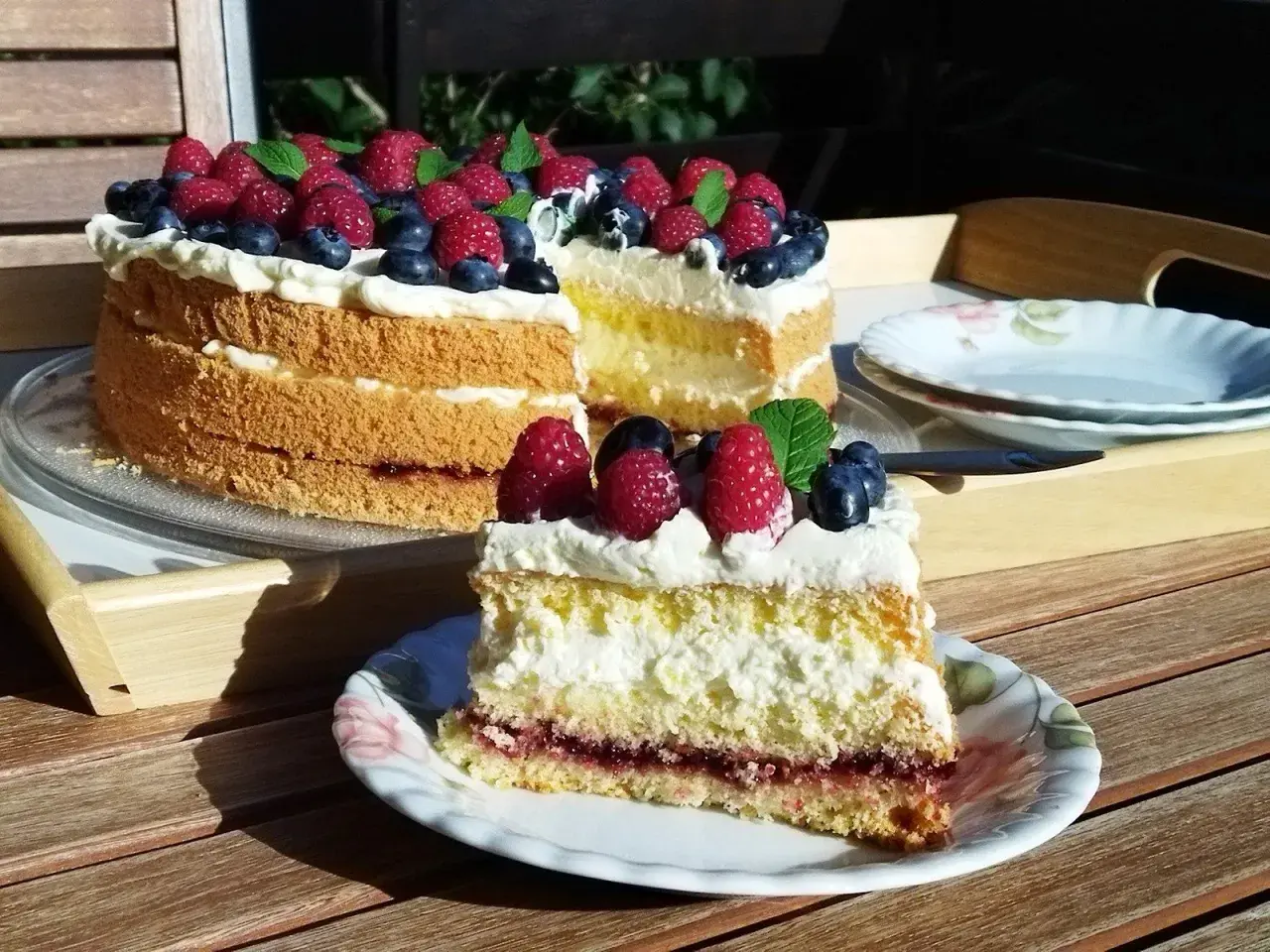 Tort biszkoptowy z kremem, malinami i borówkami, udekorowany miętą.