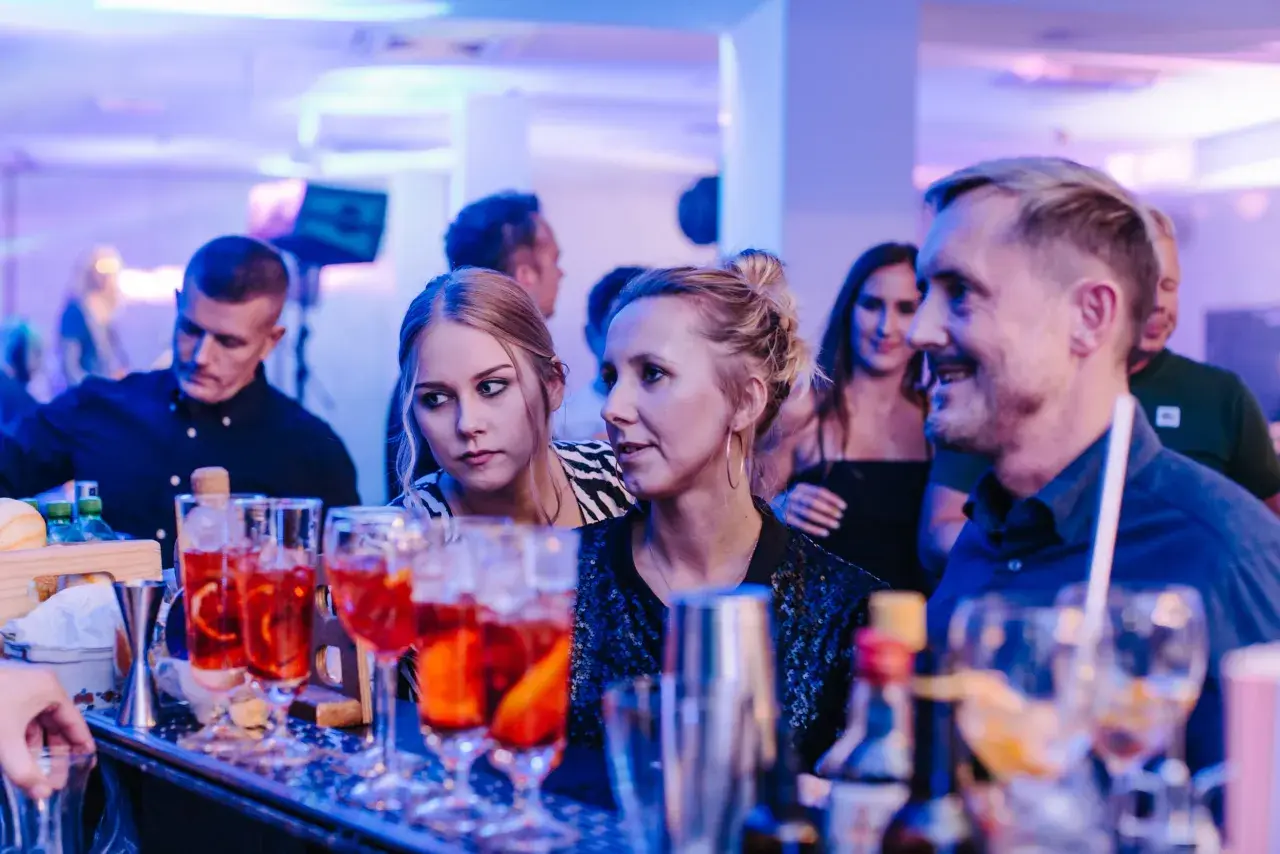Ludzie przy barze, na pierwszym planie drinki, w tle niebieskie światła.